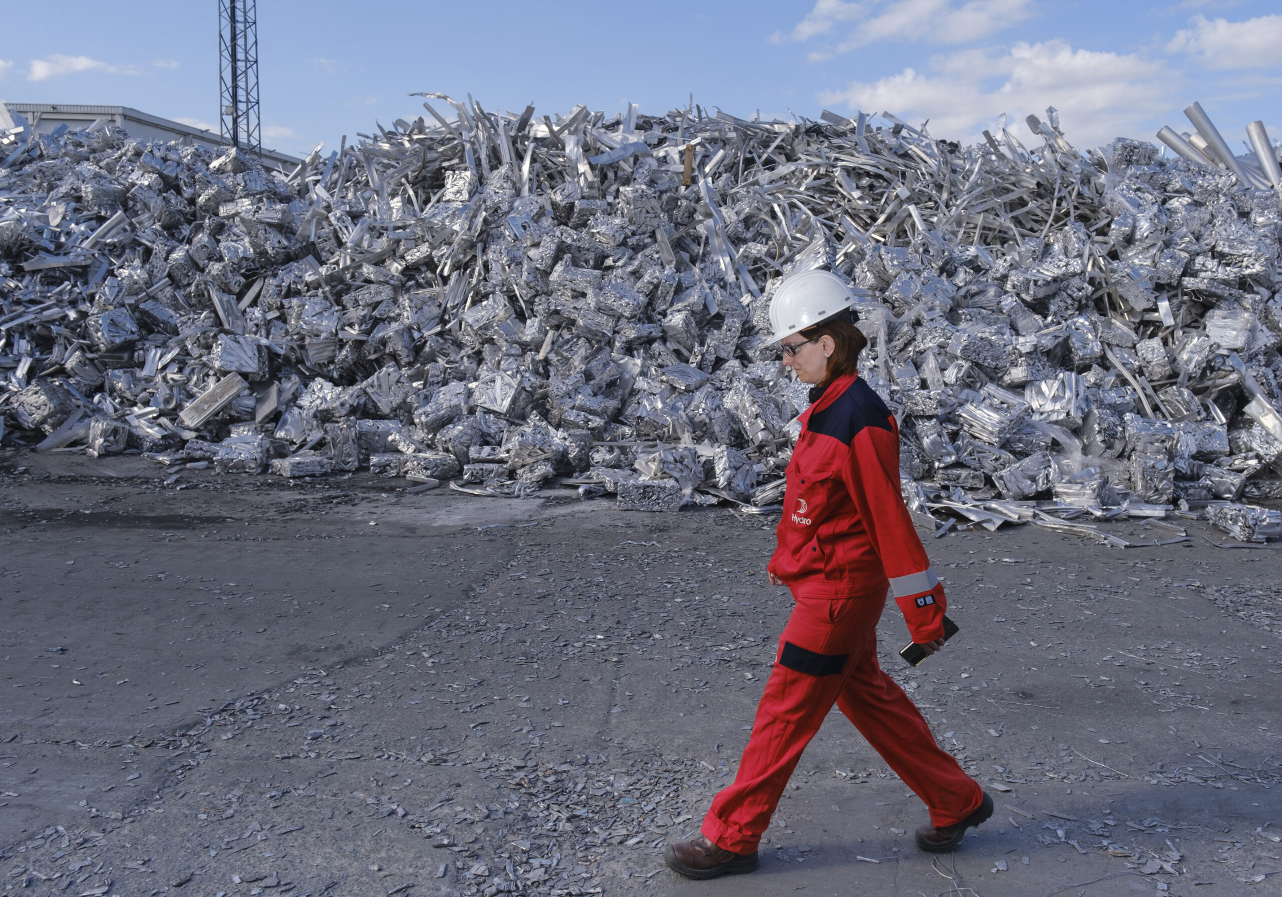 Mujer uniformada de rojo con casco caminado con fondo de basura acero